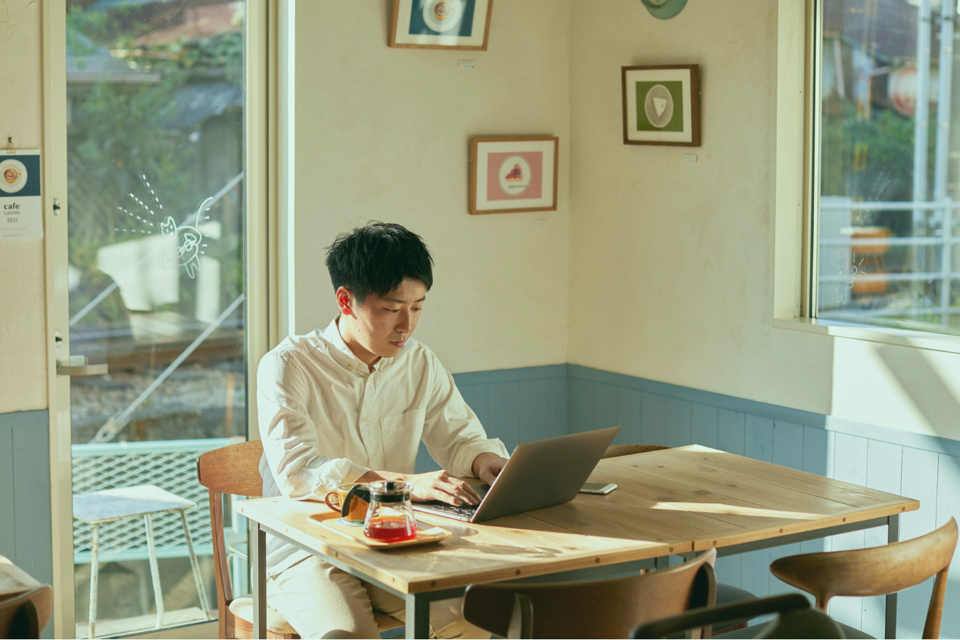 若手クリエーターが、カフェでノートPCを広げて作業している